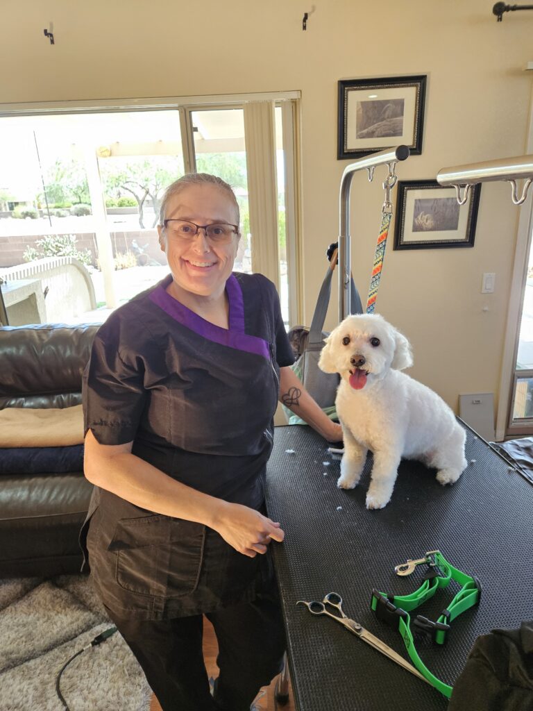 Green Dog Grooming groomer standing beside a freshly groomed small white dog on a grooming table