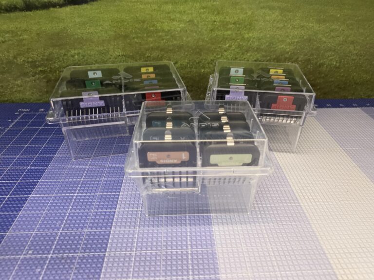 Three sets of color-coded clipper guard combs organized in clear storage cases